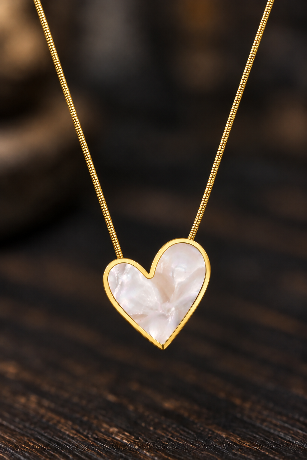 A gold heart pendant necklace with a white mother-of-pearl inlay, resting on a dark wooden surface.