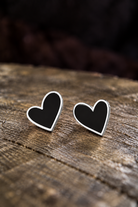 A pair of heart-shaped stud earrings with black centers and silver borders, resting on a rustic wooden surface.