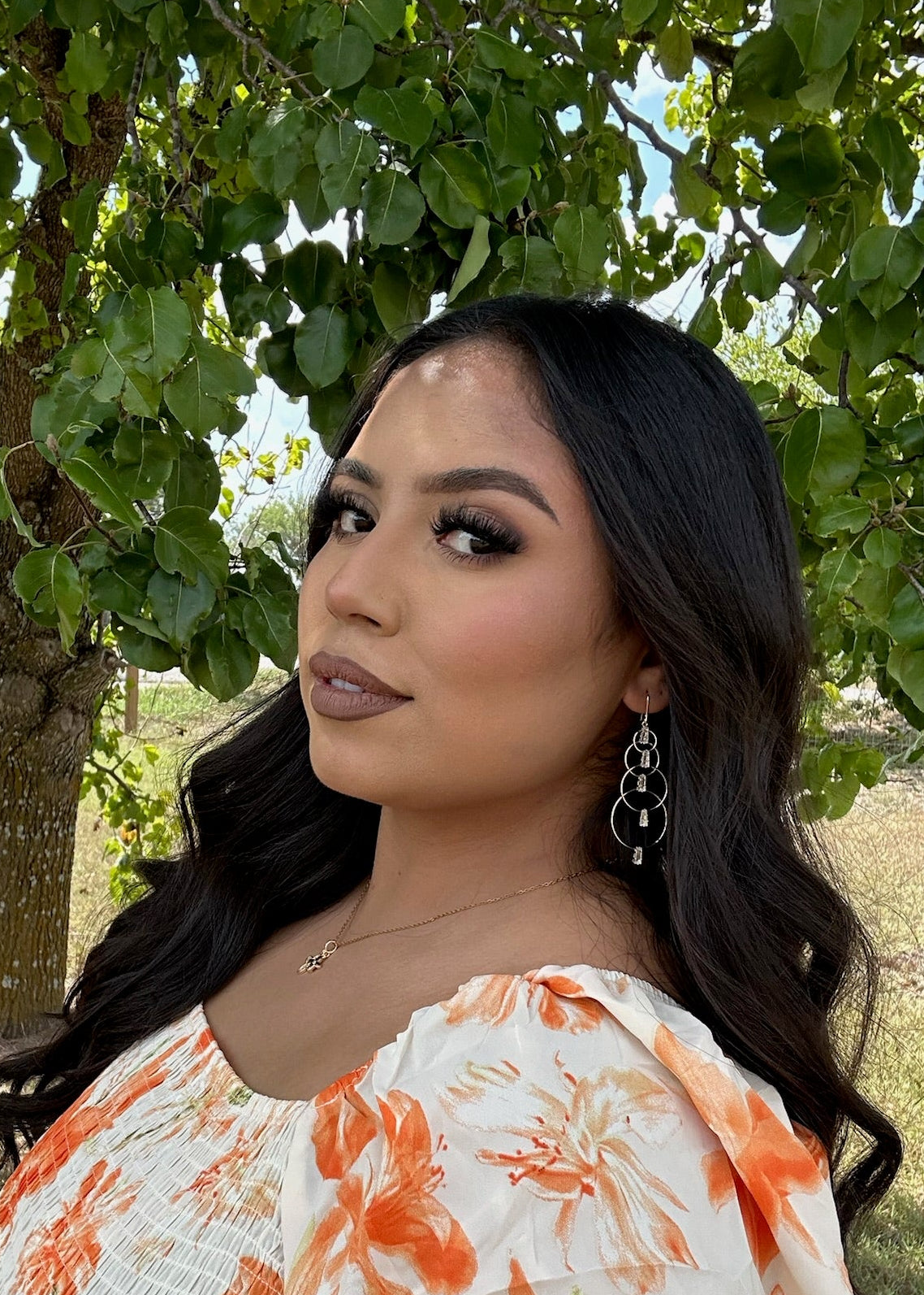Woman in a floral dress standing outdoors with trees in the background