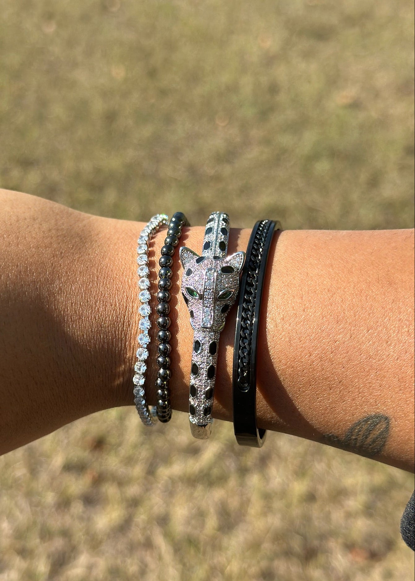 Wrist with multiple bracelets against a blurred natural background