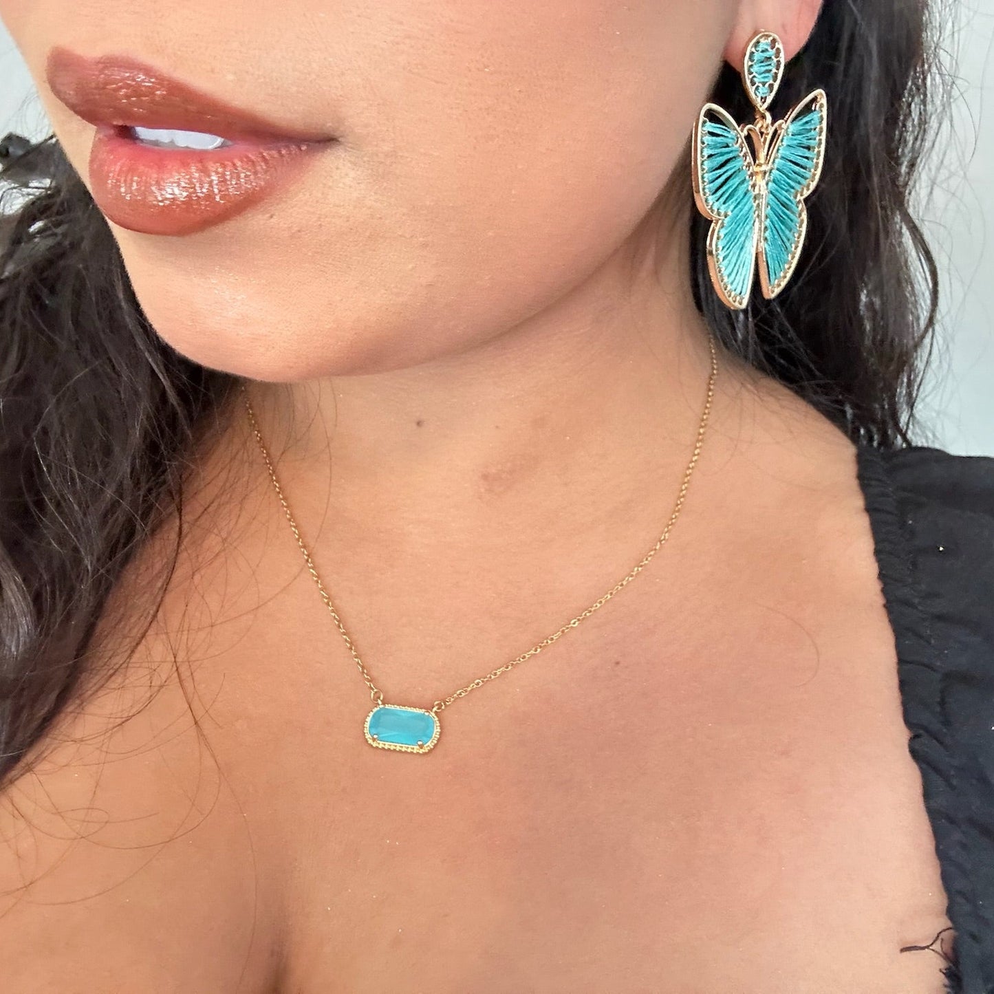 Close-up of a person wearing turquoise butterfly earrings and a matching necklace.