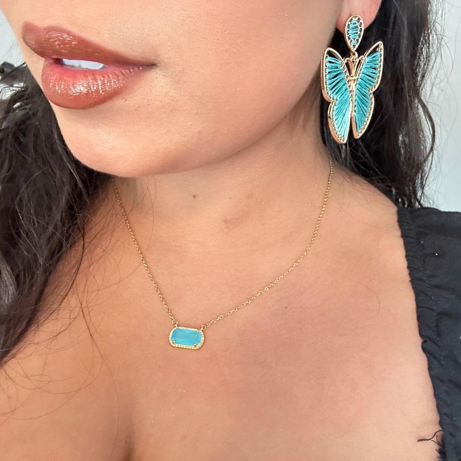 Close-up of a person wearing turquoise butterfly earrings and a matching necklace.