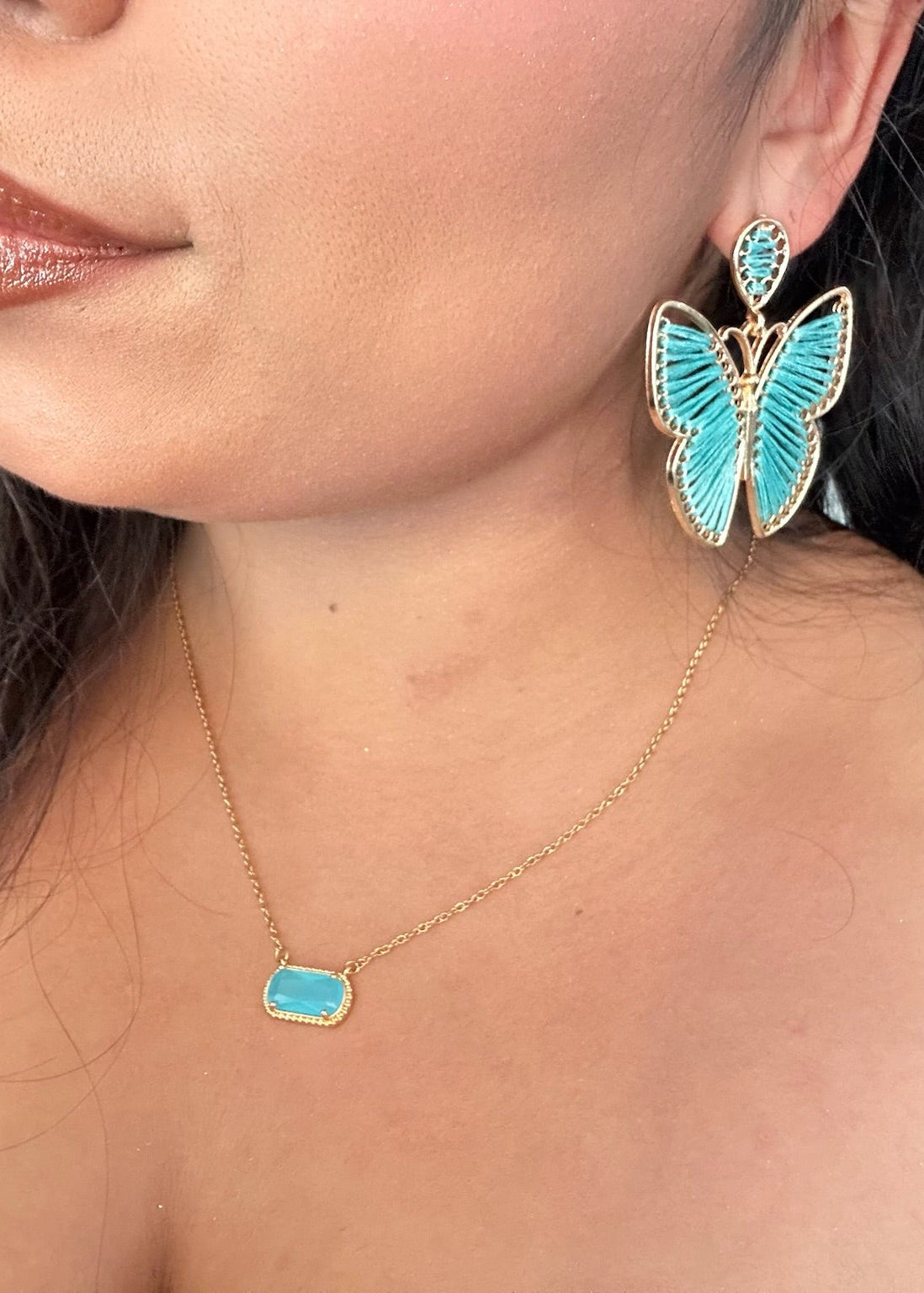 Close-up of a person wearing butterfly-shaped earrings and a necklace with turquoise stones.