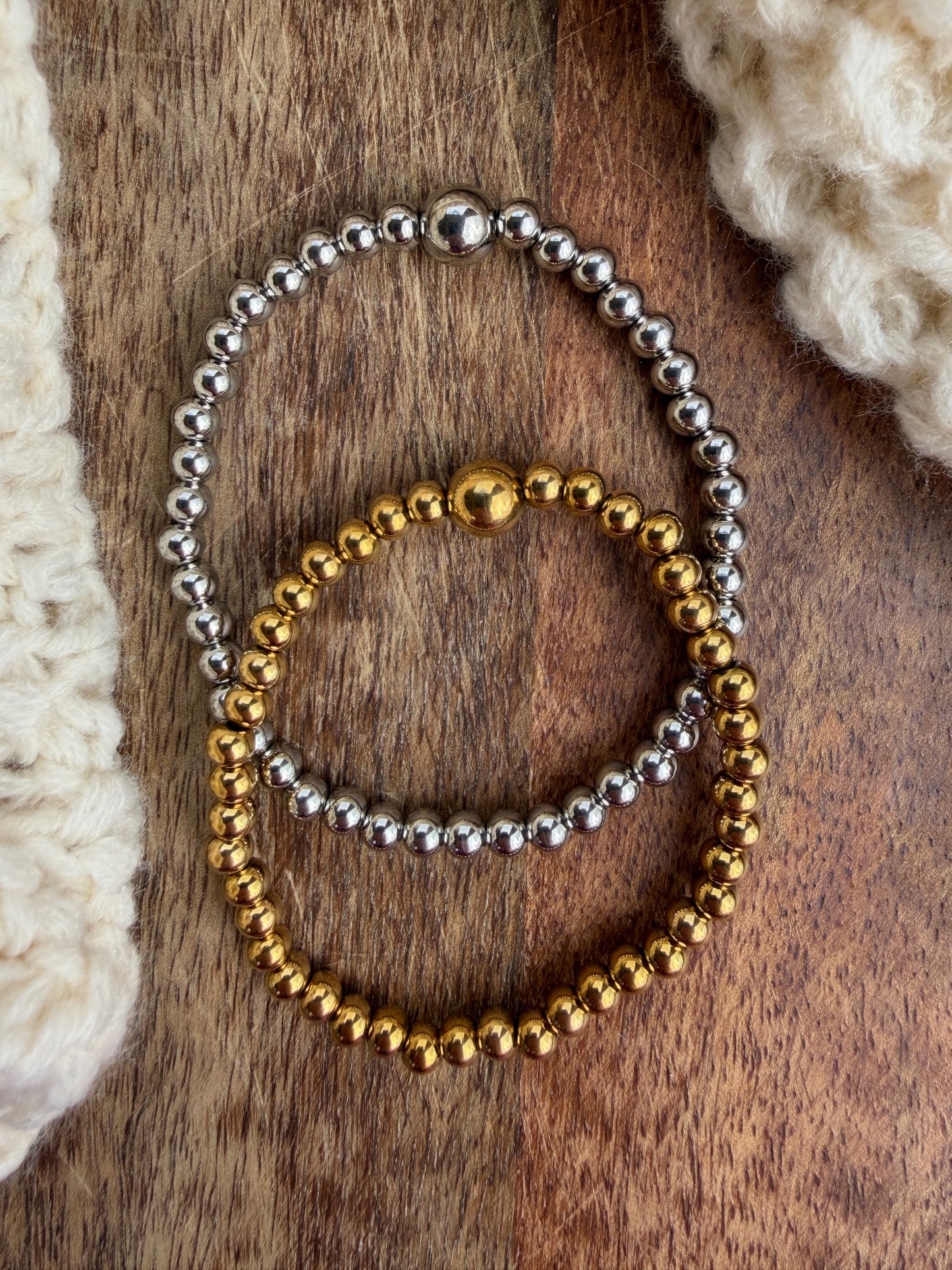 Two beaded bracelets, one silver and one gold, on a wooden surface.