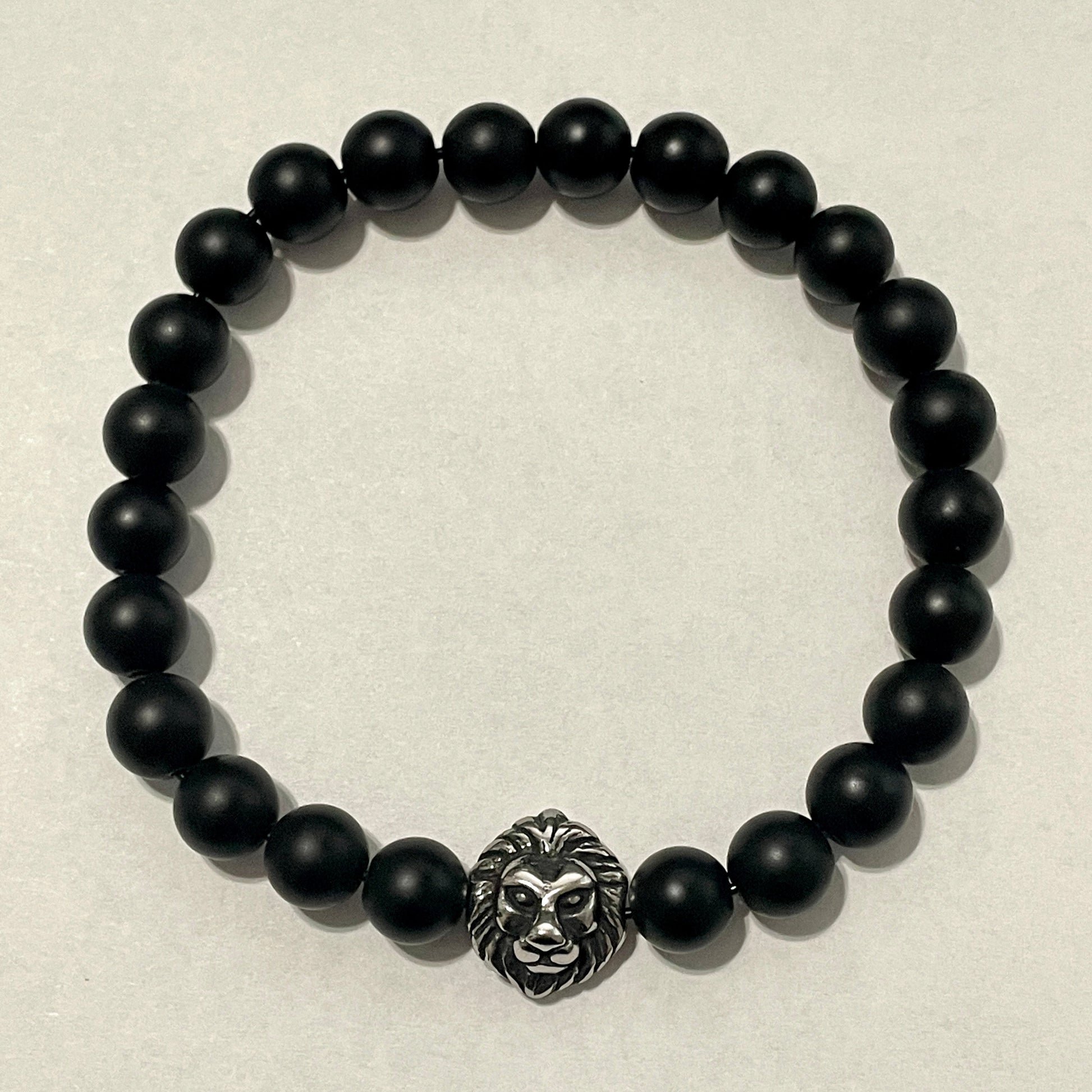 Black beaded bracelet with a lion head charm on a beige background