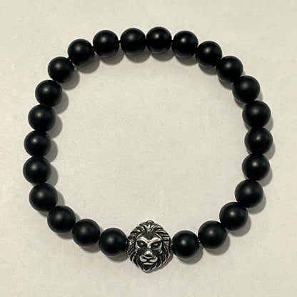 Black beaded bracelet with a lion head charm on a beige background
