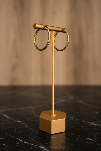 Lupita Hoops featuring twisted gold hoop earrings crafted from stainless steel with 18kt gold plating displayed on a jewelry stand.