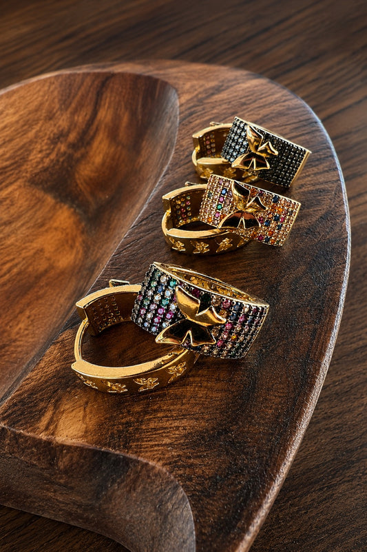 Three gold-toned rings with star-shaped crystal pavé bands, displayed on a carved wooden serving board.