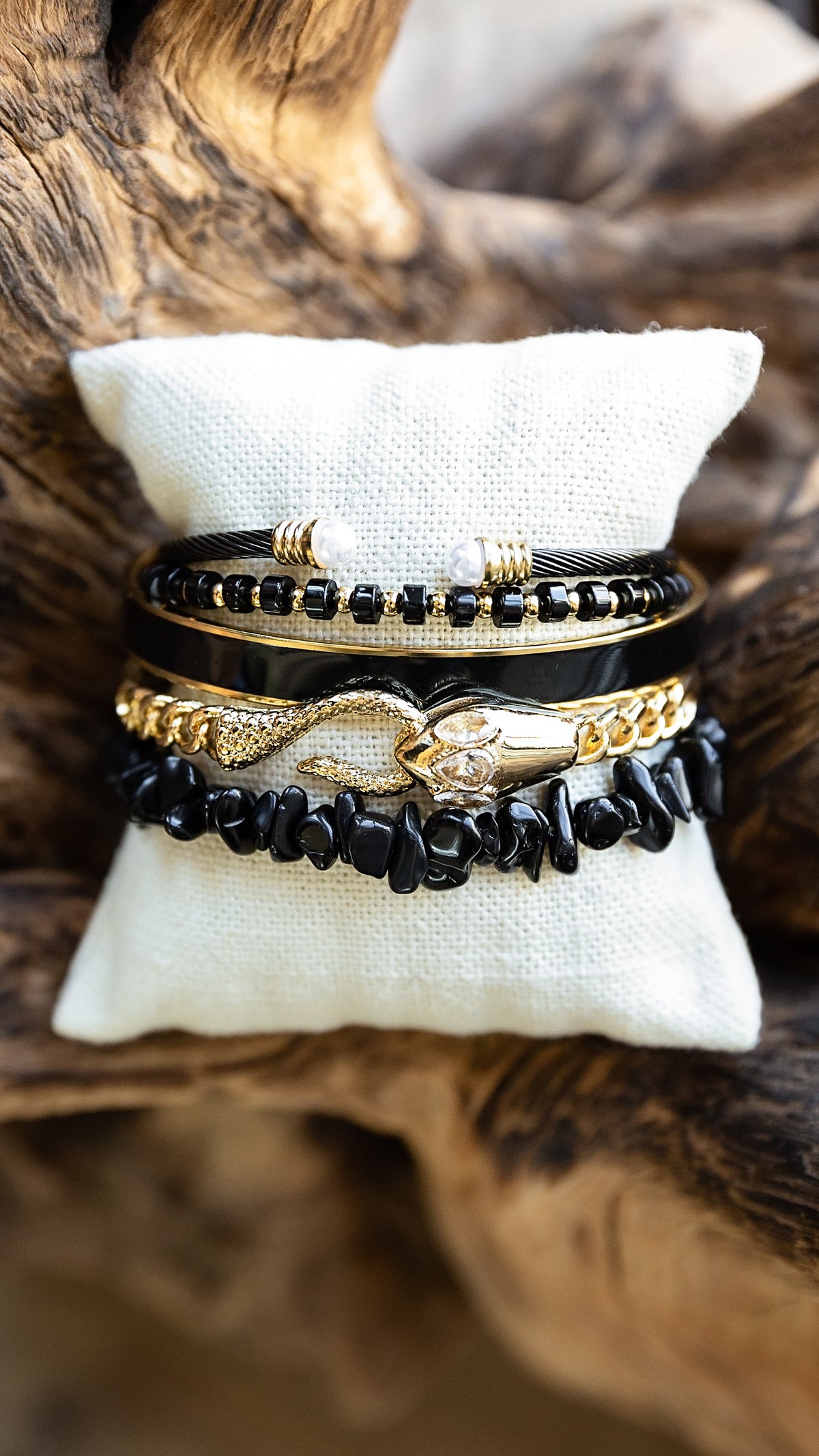 Noir Bracelet featuring genuine black obsidian stones and gold-tone details styled on a jewelry display pillow.