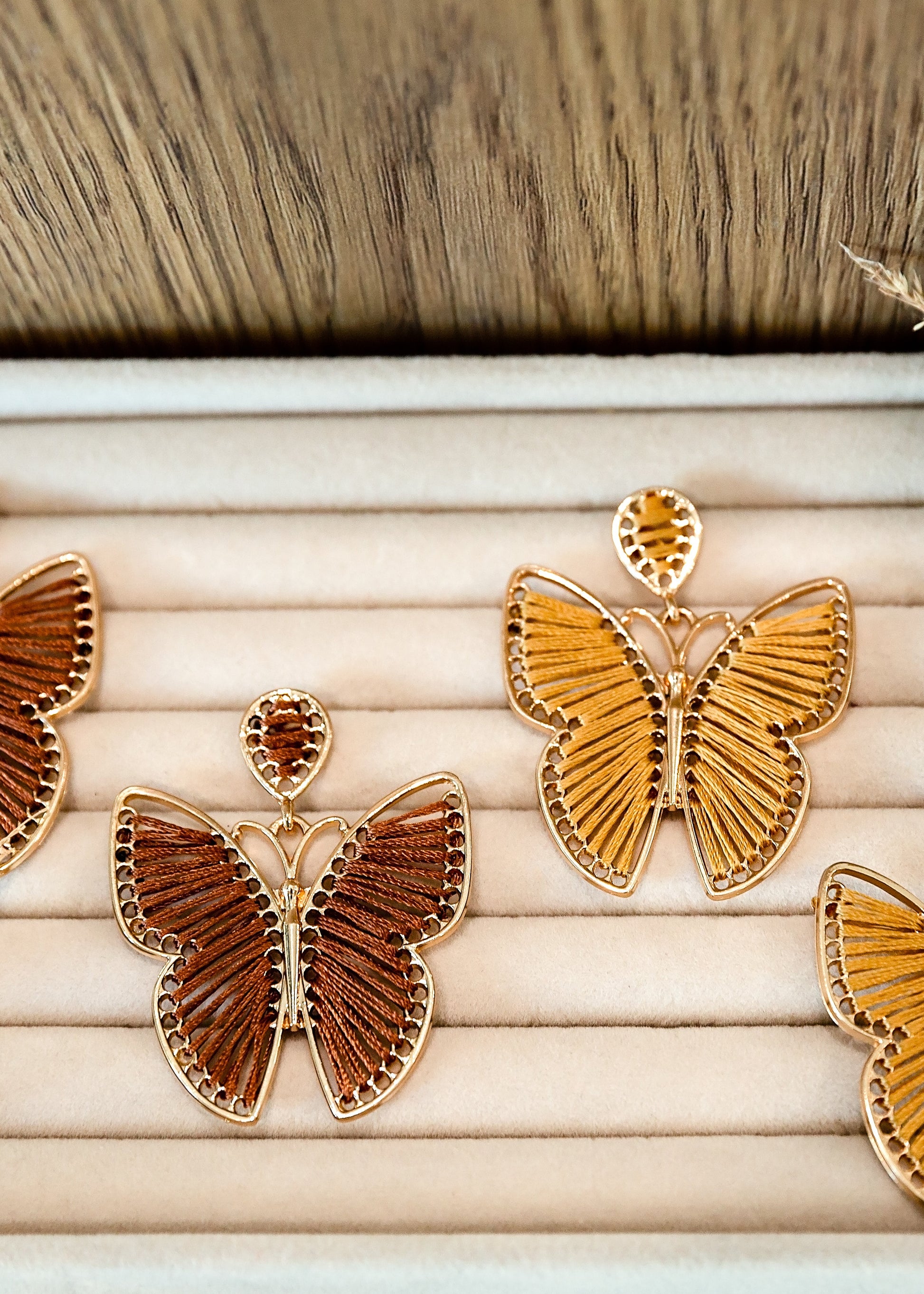 Butterfly-shaped earrings on a wooden tray with a natural background