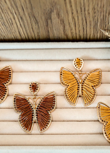 Butterfly-shaped earrings on a wooden tray with a natural background