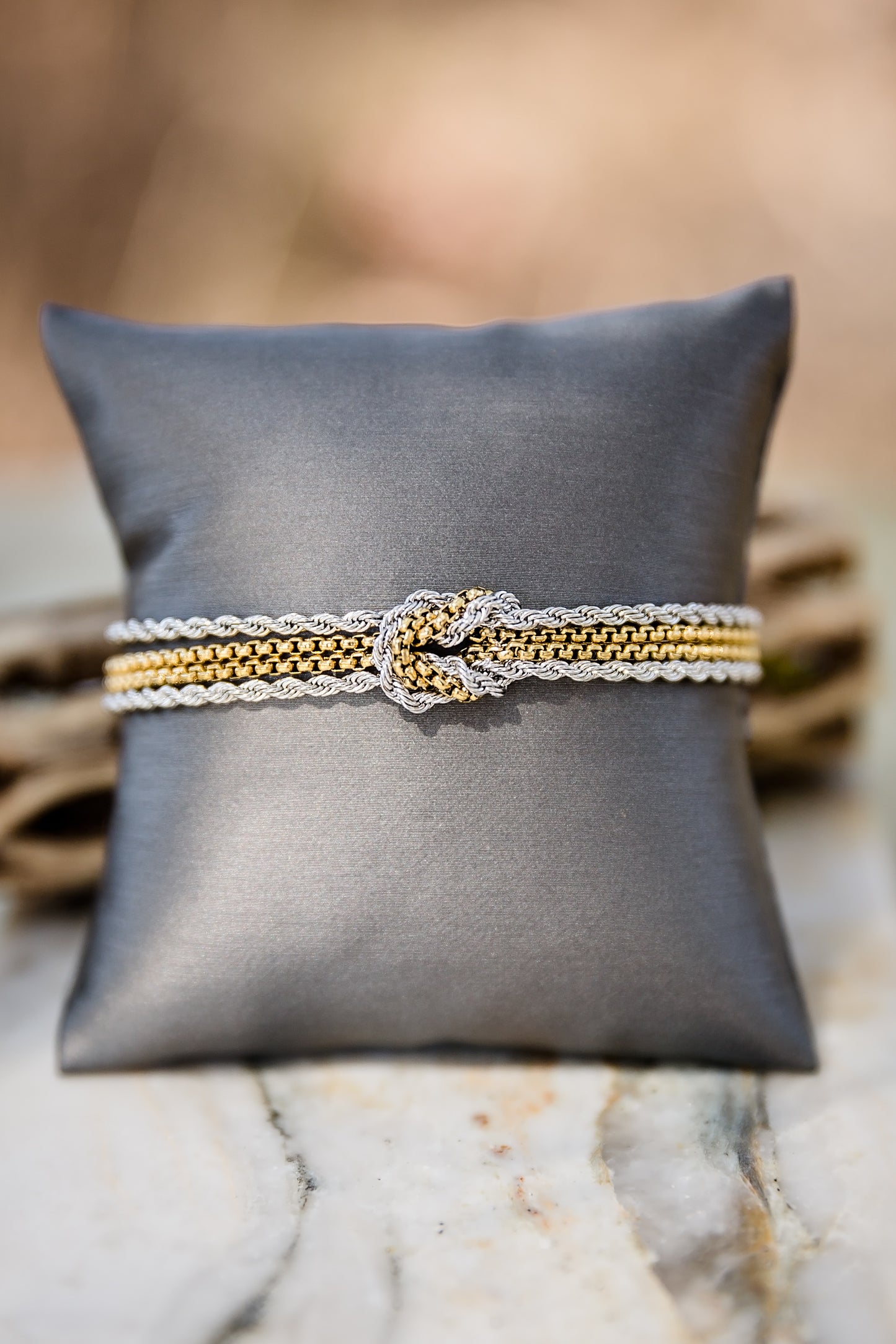 Mixed metal Parker bracelet with gold and silver tones displayed on a black pillow, featuring layered chain design and central detail