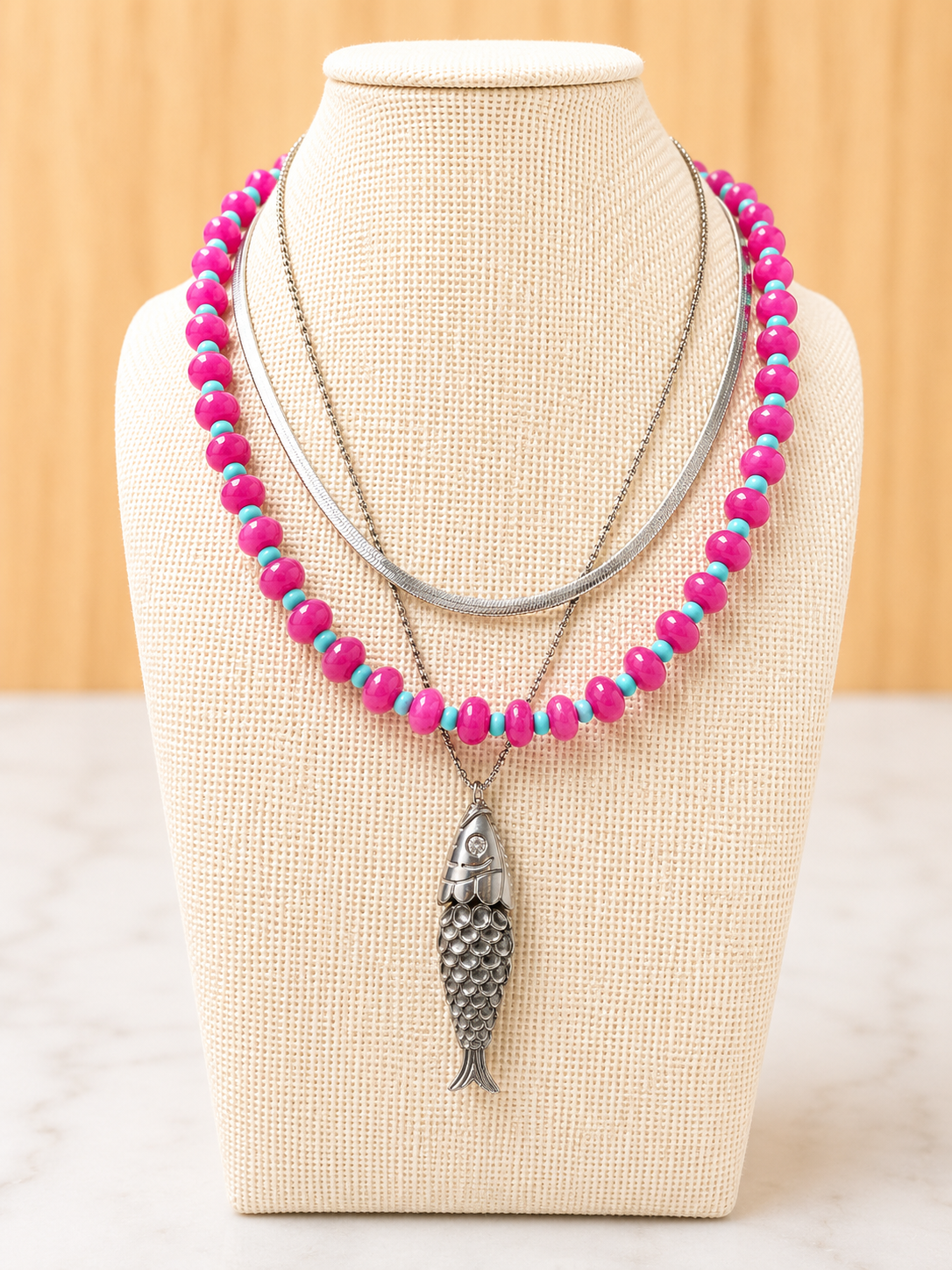 Pesce d'Oro Necklace layered with colorful beaded necklaces, showcasing its textured fish pendant and effortless coastal-inspired style.