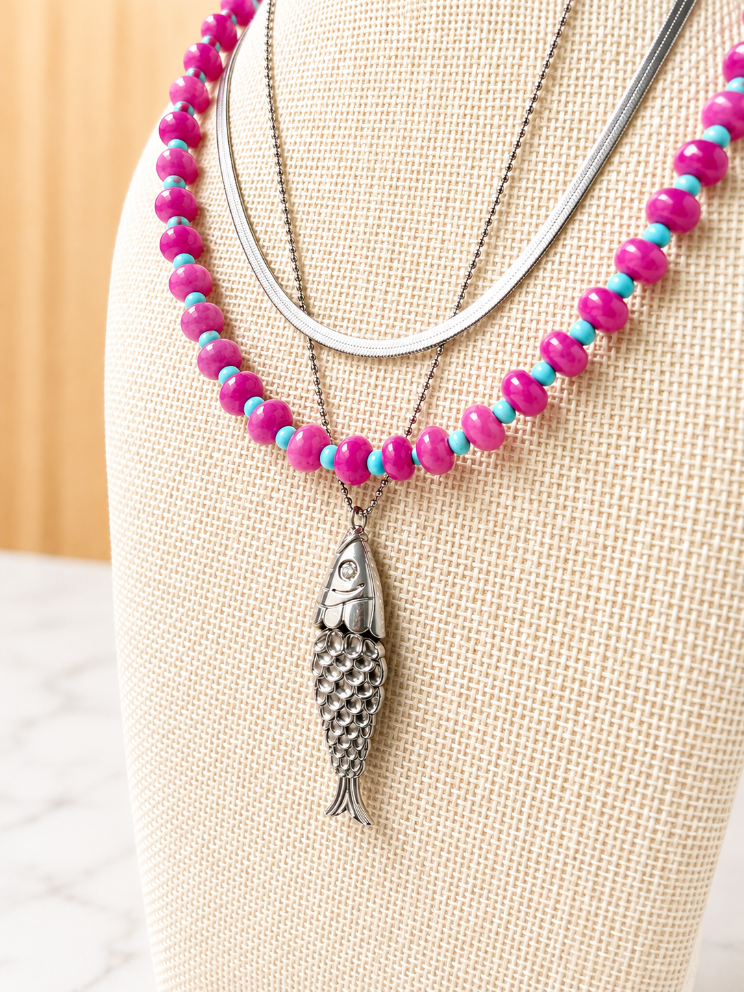 Pesce d'Oro Necklace layered with colorful beaded necklaces, showcasing its textured fish pendant and effortless coastal-inspired style.