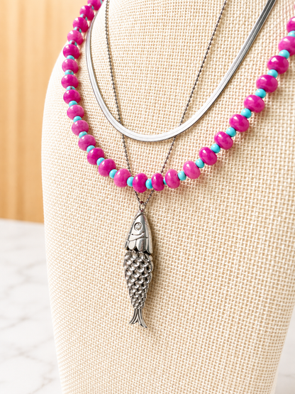 Pesce d'Oro Necklace layered with colorful beaded necklaces, showcasing its textured fish pendant and effortless coastal-inspired style.