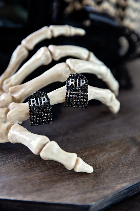 RIP Earrings by VEITA Jewelry featuring miniature black tombstone designs with sparkling black crystals and RIP lettering, displayed beneath a decorative skeleton hand.