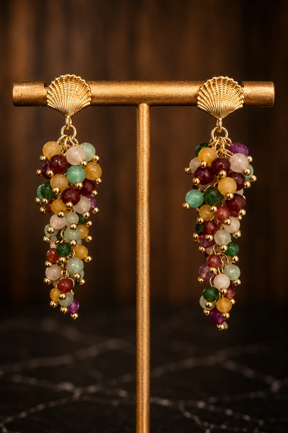 Close-up of Raelynn gemstone cascade earrings with multicolored natural gemstones and 18kt gold-plated shell posts.