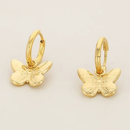 Gold butterfly earrings on a light beige background