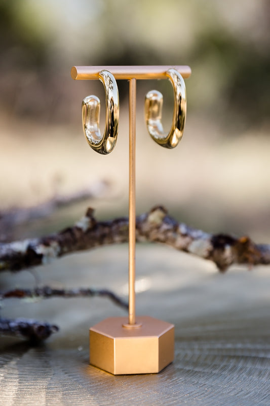 Gold high polish sculptural hoop earrings displayed on stand