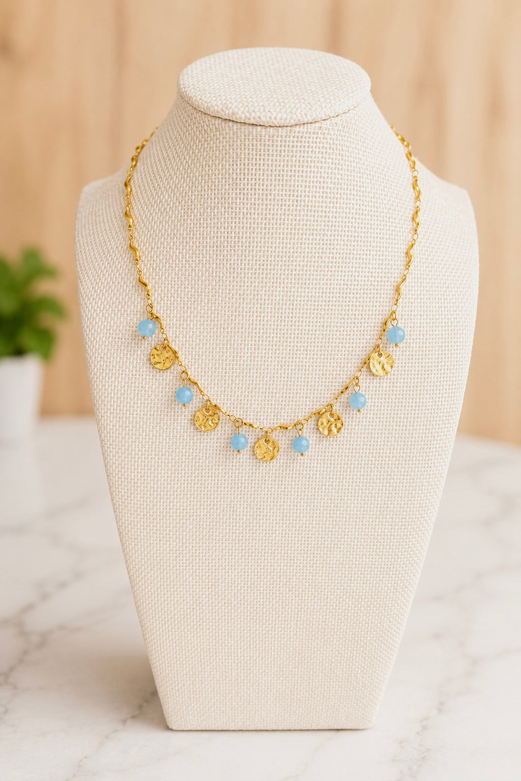 Seaside Necklace displayed on a jewelry bust, showcasing hand-beaded blue accents and an 18kt gold plated chain.