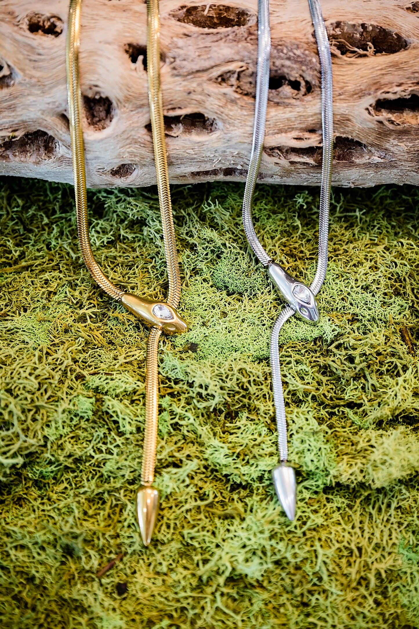 Gold and silver serpentine-style necklaces with sleek curved design displayed on moss background