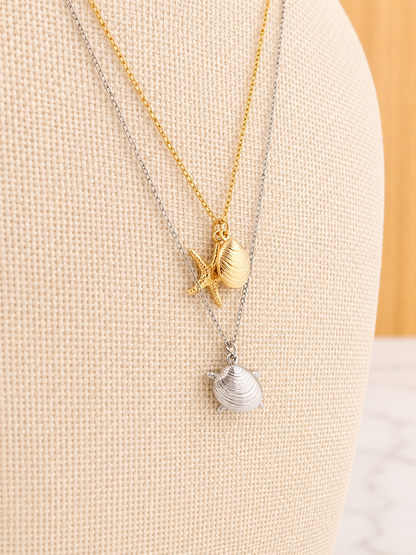 Shoreline Necklace featuring delicate shell and starfish charms on an 18kt gold plated stainless steel chain with a coastal-inspired design.