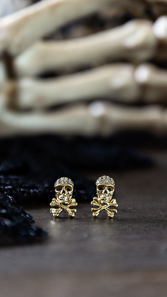 Gold plated Skull Micro Stud Earrings by VEITA Jewelry featuring miniature skull designs with sparkling crystal accents, displayed against a dark background.
