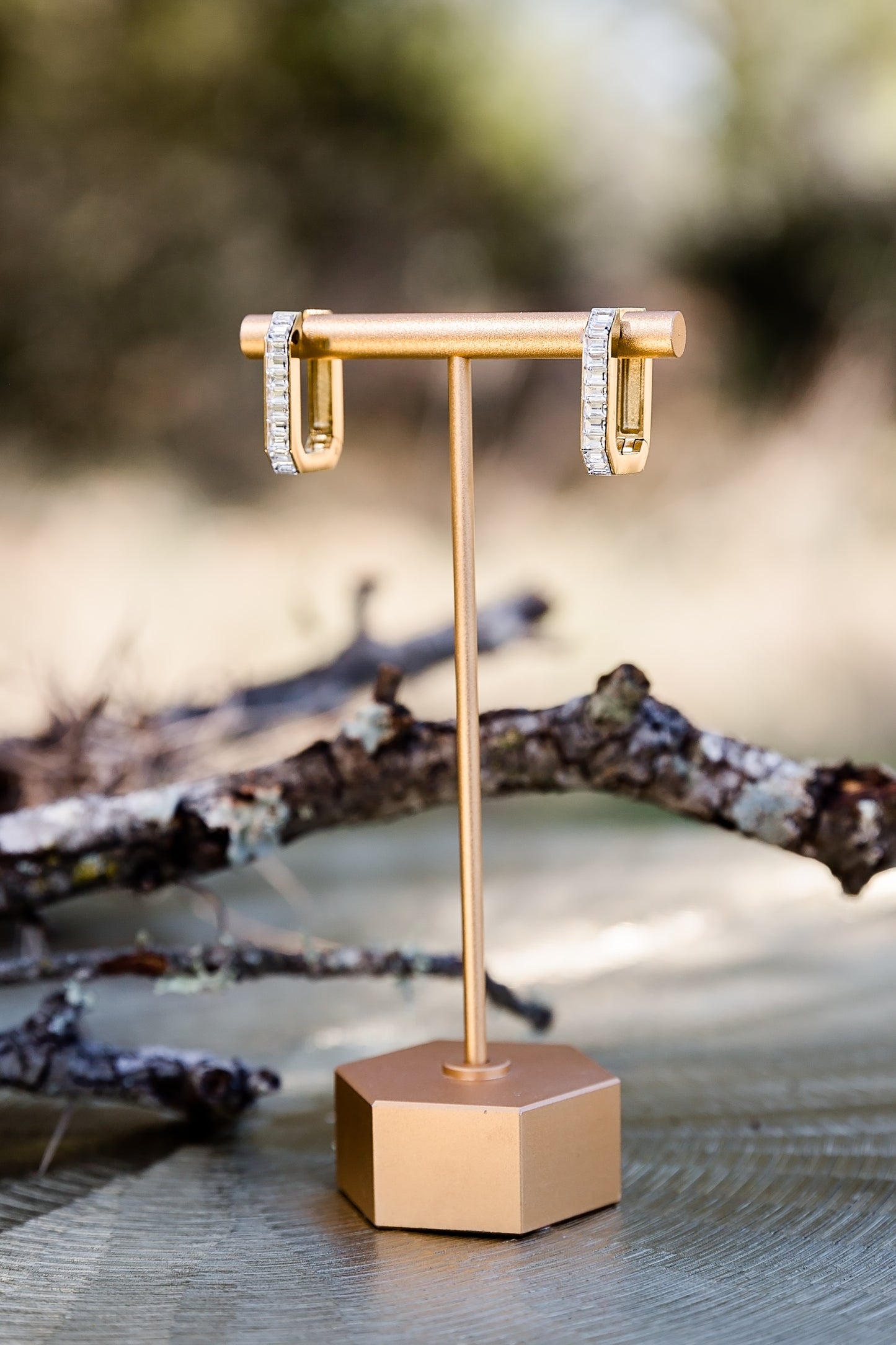 Sloane hoop earrings displayed on a jewelry stand outdoors, highlighting sleek shape and polished finish
