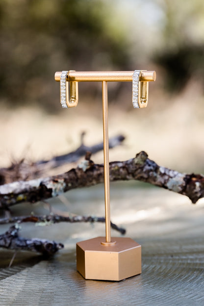 Sloane hoop earrings displayed on a jewelry stand outdoors, highlighting sleek shape and polished finish