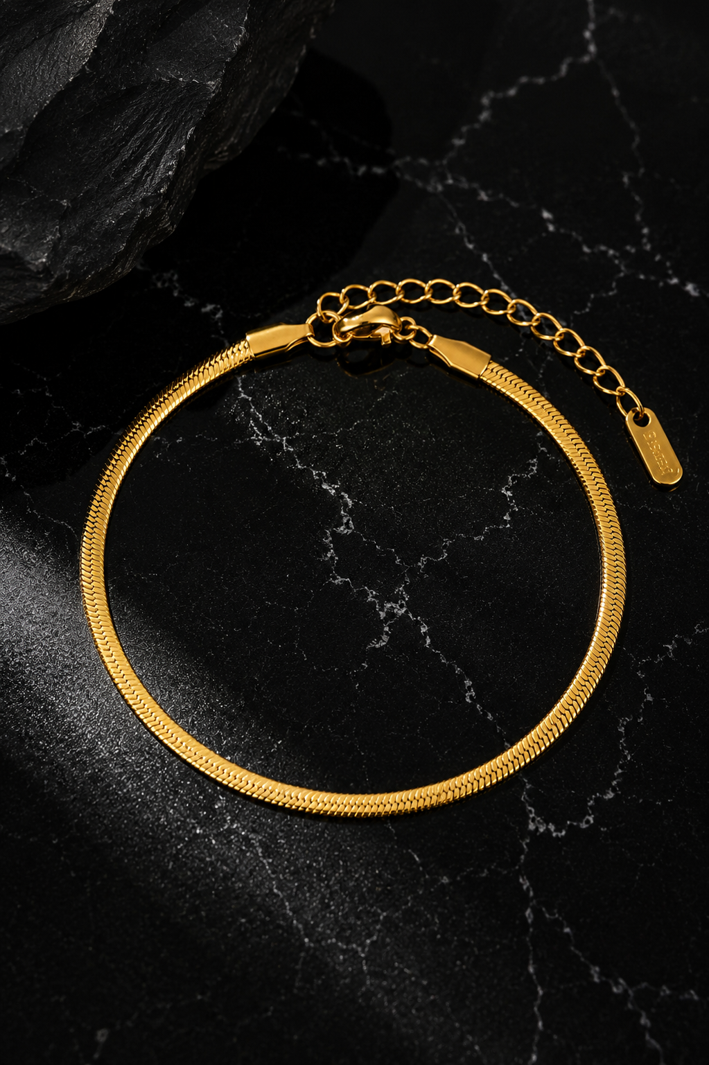 Snake Chain Anklet featuring a flat stainless steel snake chain with 18kt gold plating displayed on a black background.