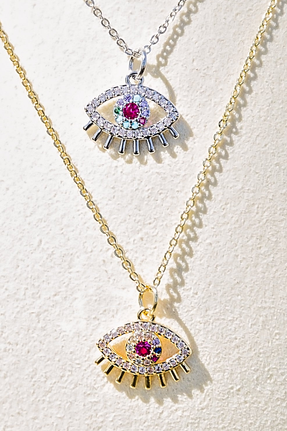 Spectral eye necklace featuring gold and silver evil eye pendants with multicolor zircon stones displayed in layered styling closeup
