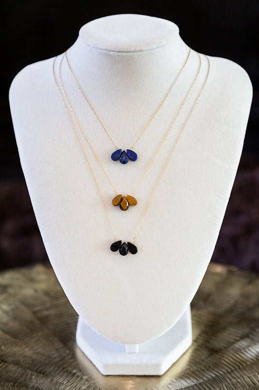 Trine Necklace with three layered gold chains and blue, amber and black gemstone drops displayed on a white jewelry bust.