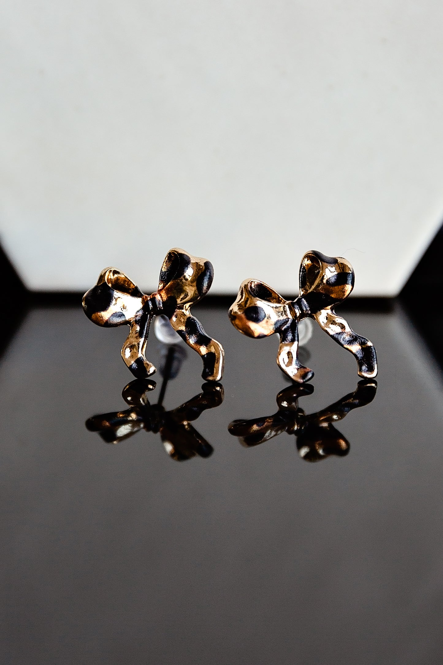Gold leopard print bow stud earrings on a reflective surface with a gray background