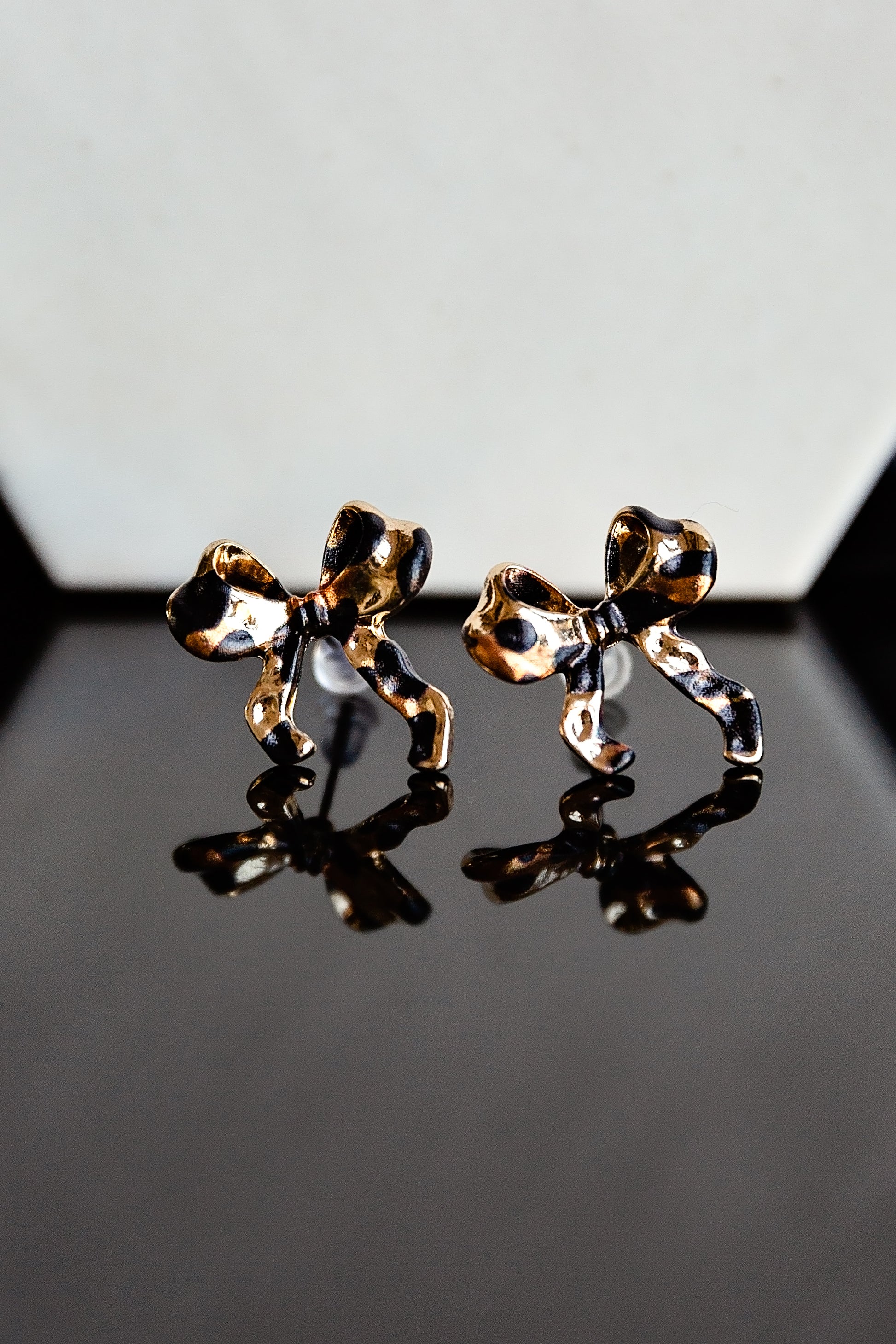 Gold leopard print bow stud earrings on a reflective surface with a gray background