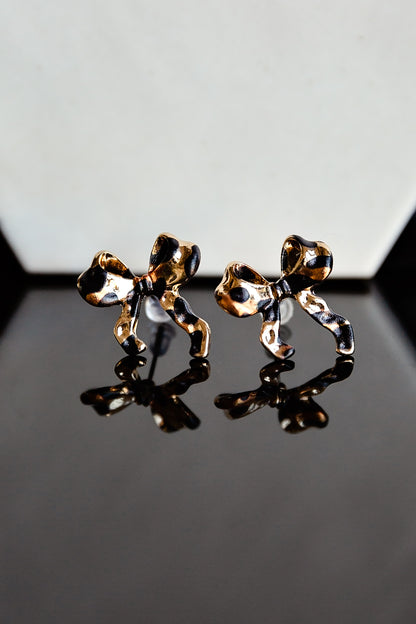 Gold leopard print bow stud earrings on a reflective surface with a gray background