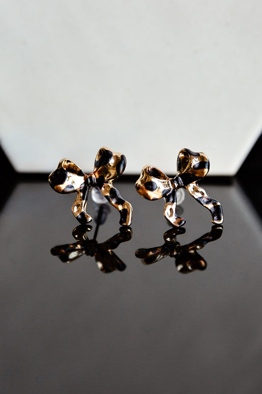Gold leopard print bow stud earrings on a reflective surface with a gray background