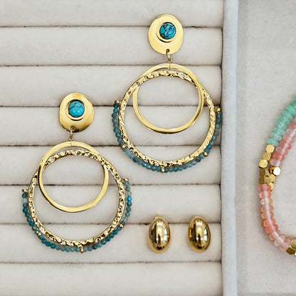 Gold and turquoise hoop earrings on a textured surface