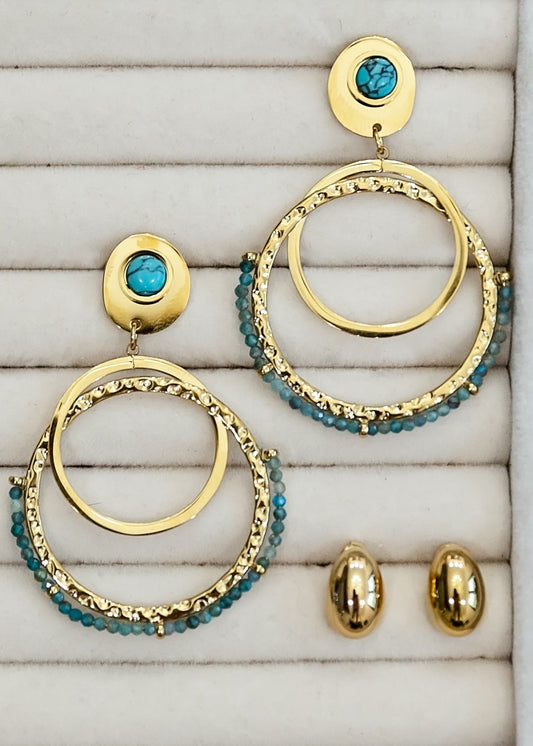 Gold and turquoise hoop earrings on a textured surface