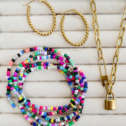 Gold hoop earrings, colorful beaded bracelets, and a gold chain necklace on a wooden surface.
