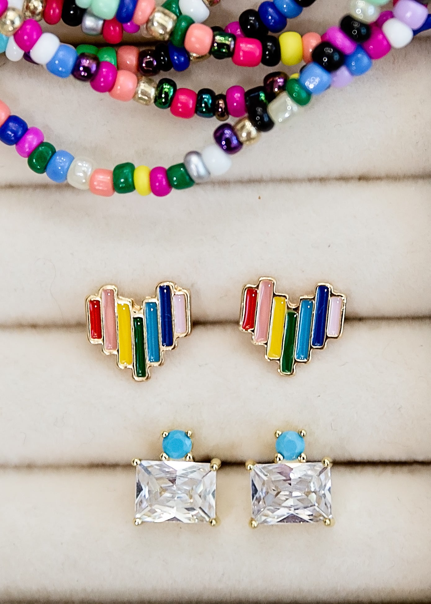 Colorful beaded bracelets and rainbow-stud earrings on a wooden surface