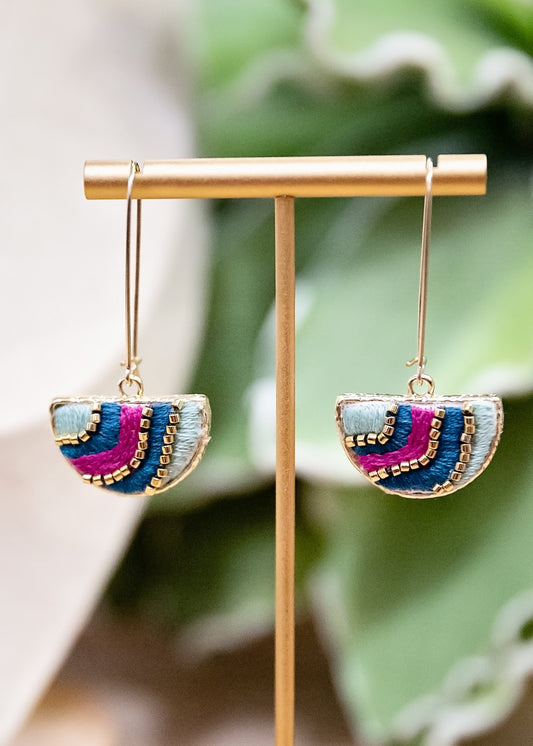 Colorful earrings on a gold earring stand with a green leafy background