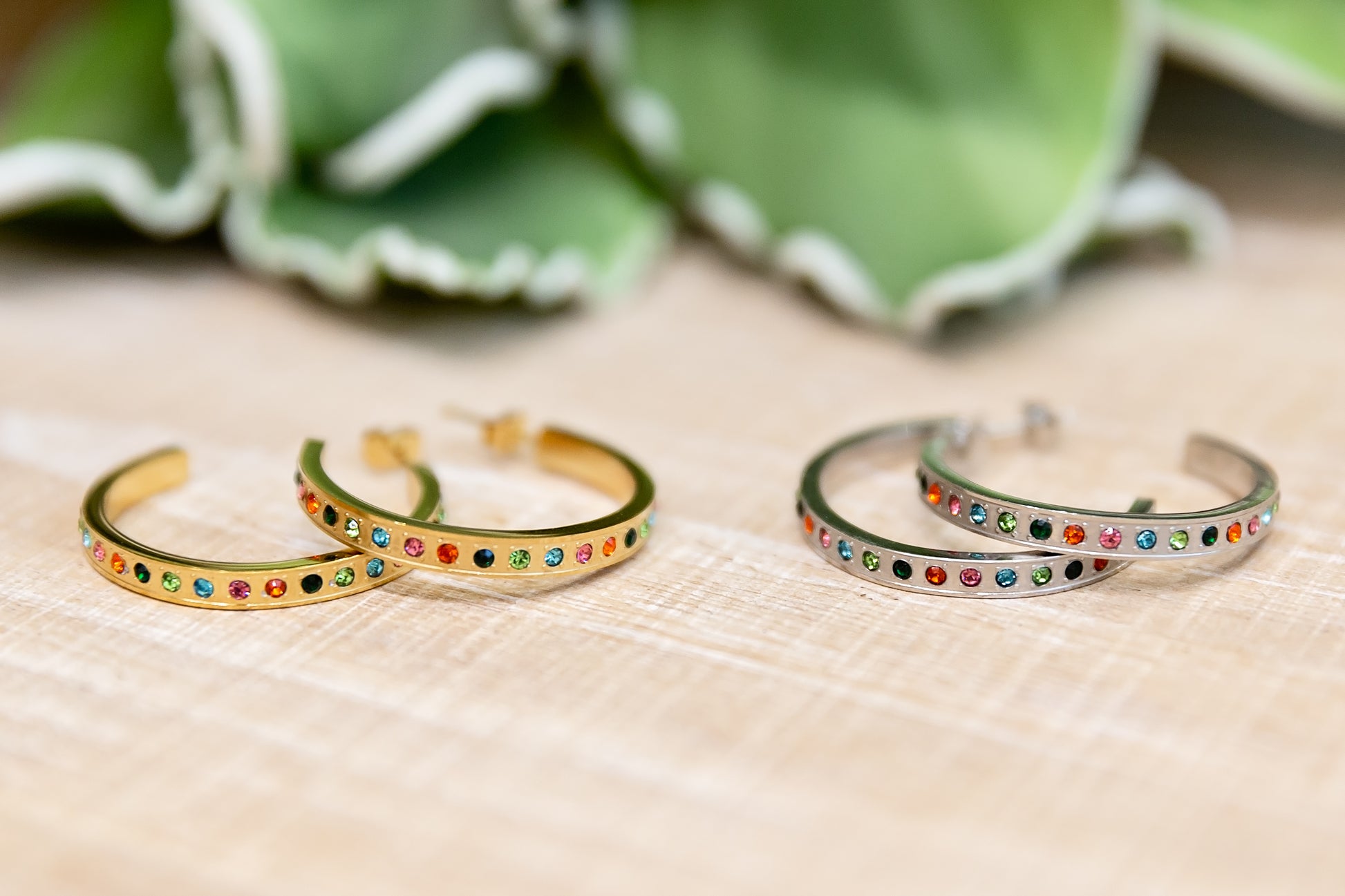 Two gold and silver bangles with colorful stones on a beige surface.
