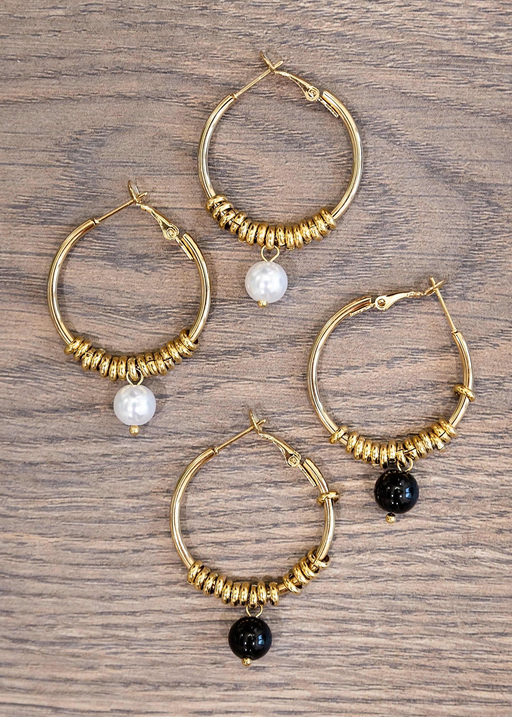 Set of gold hoop earrings with beads on a wooden surface