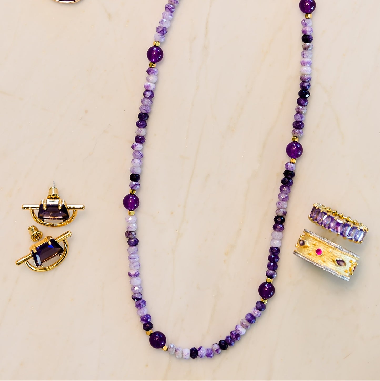 Purple beaded necklace and earrings on a beige background