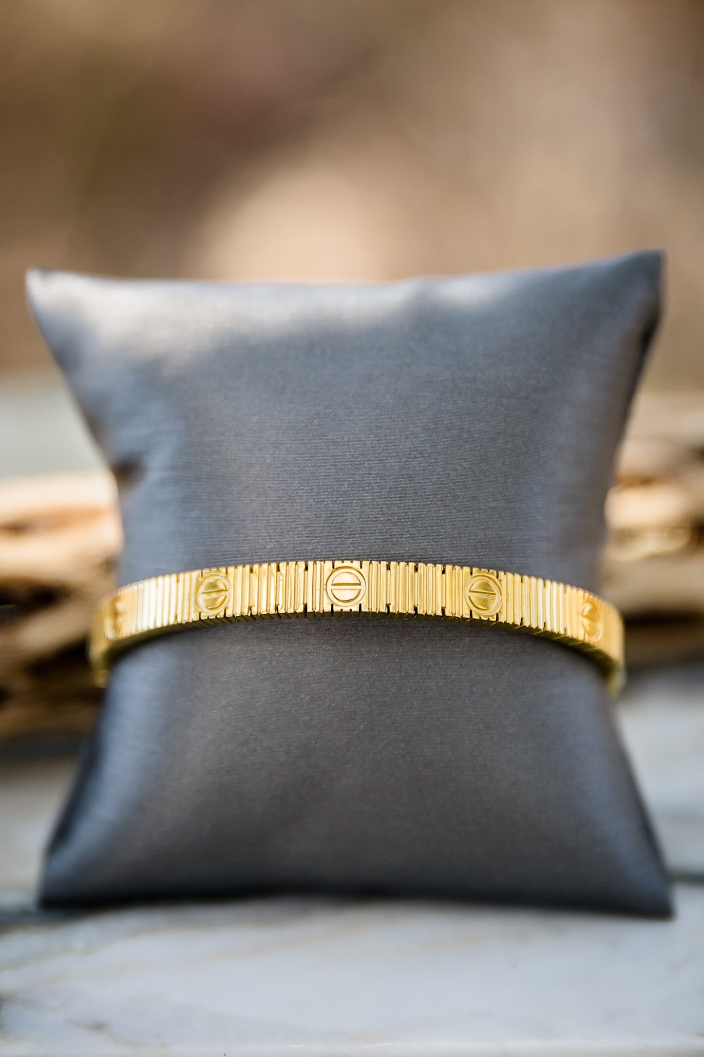 Vesper textured gold bangle bracelet on display pillow featuring stainless steel with 18kt gold plating and hinged design