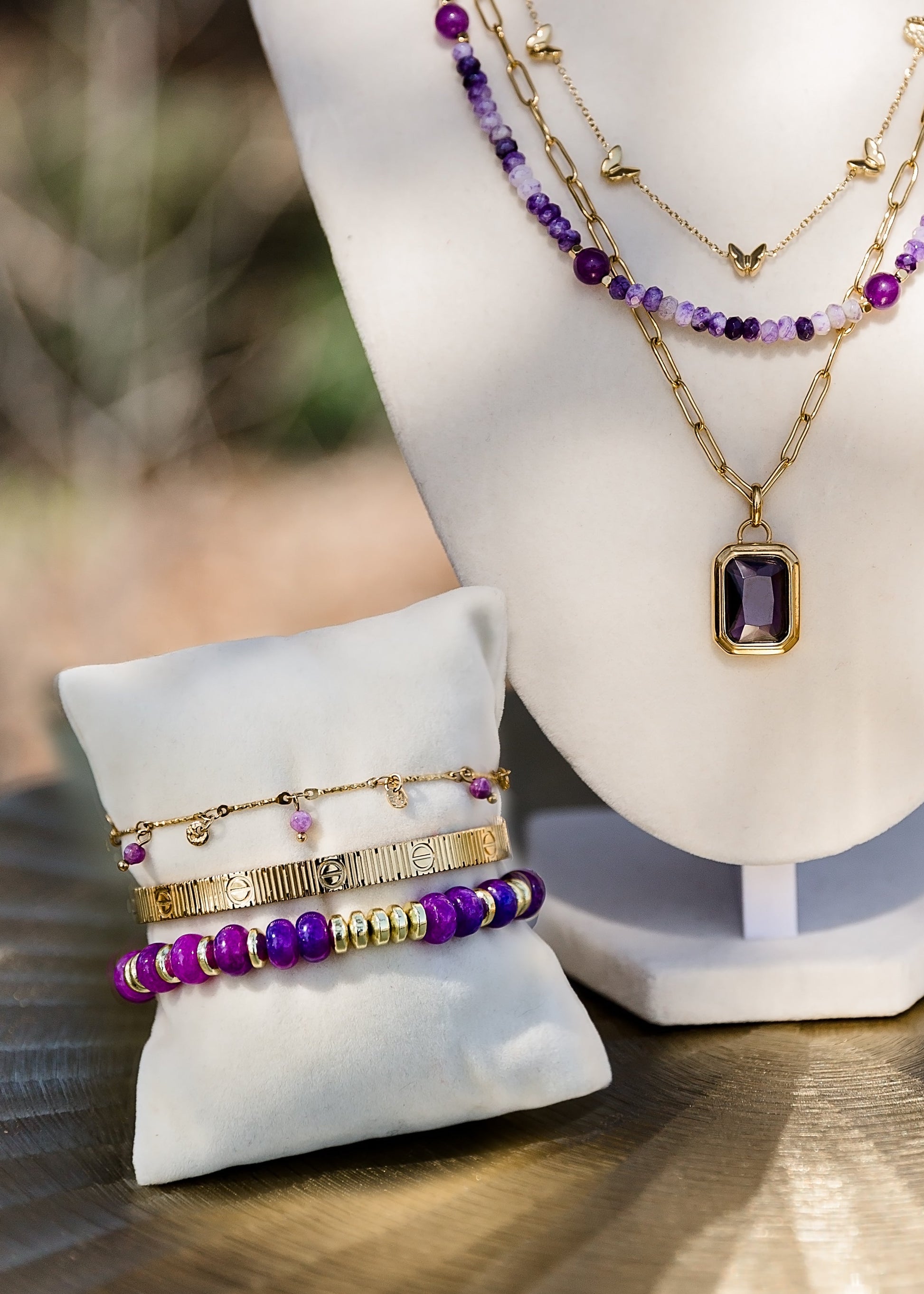 Jewelry set including necklaces, bracelets, and earrings on a mannequin and stand outdoors.
