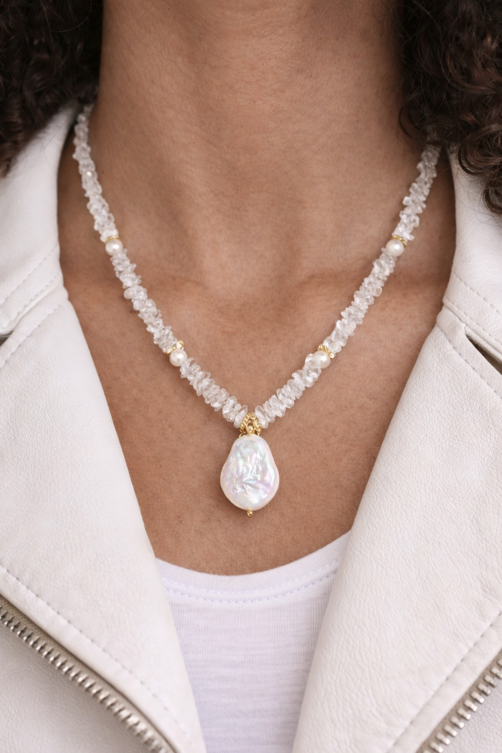 Pearl necklace with a pendant worn by a person in a white jacket.