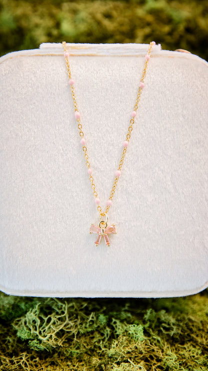 Ava Bow Necklace in gold with textured chain and pink glass bow charm featuring peachy pink bead detail
