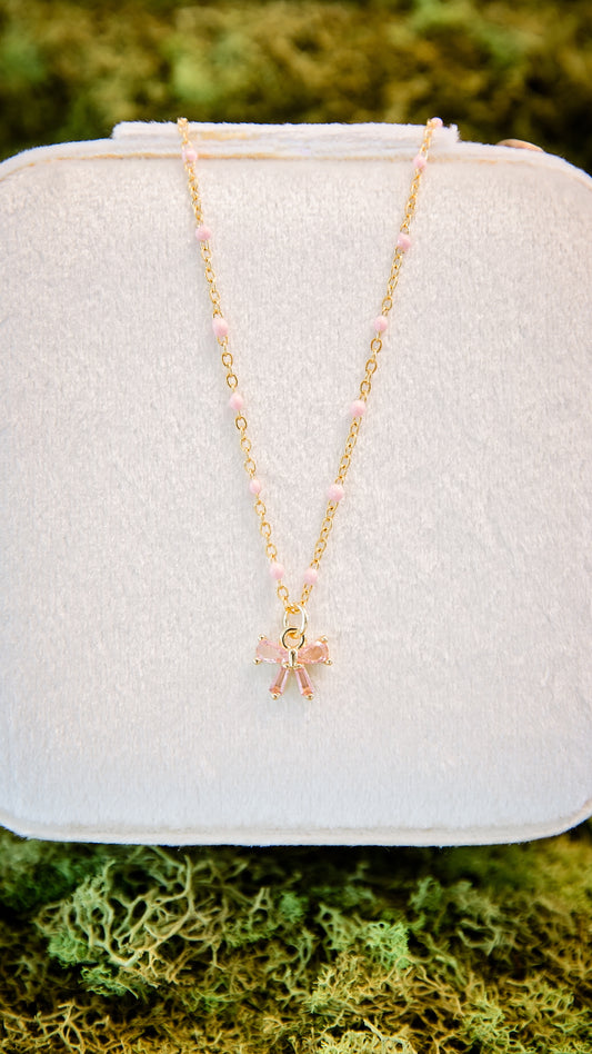 Ava Bow Necklace in gold with textured chain and pink glass bow charm featuring peachy pink bead detail