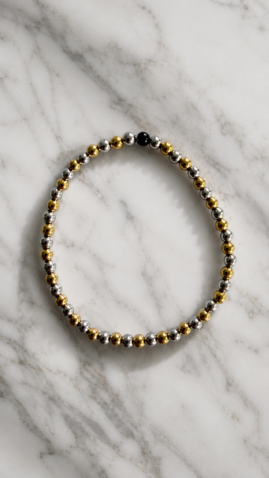Beaded bracelet with gold, silver, and black beads on a marble surface